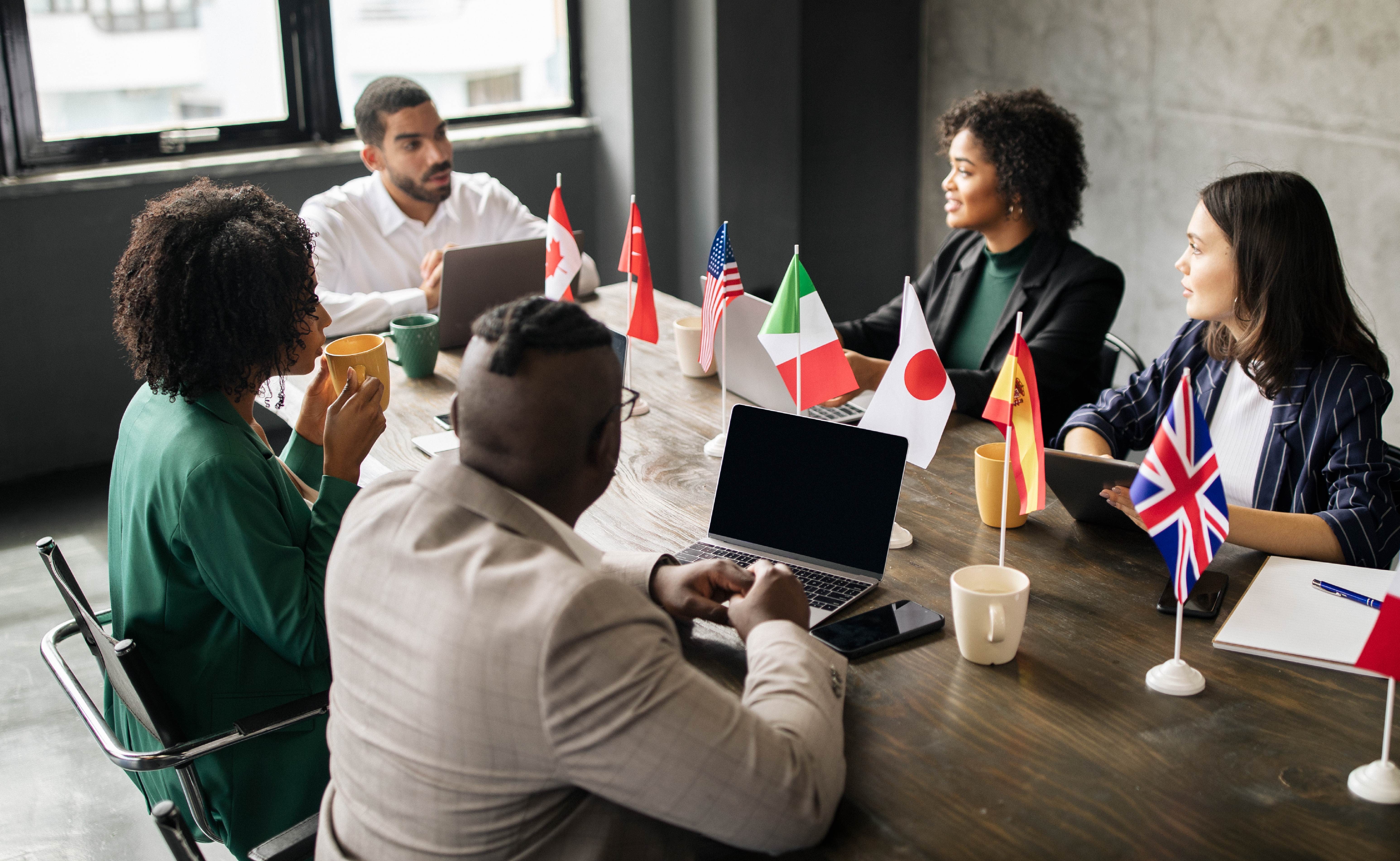 An international team meeting around a table with national flags.