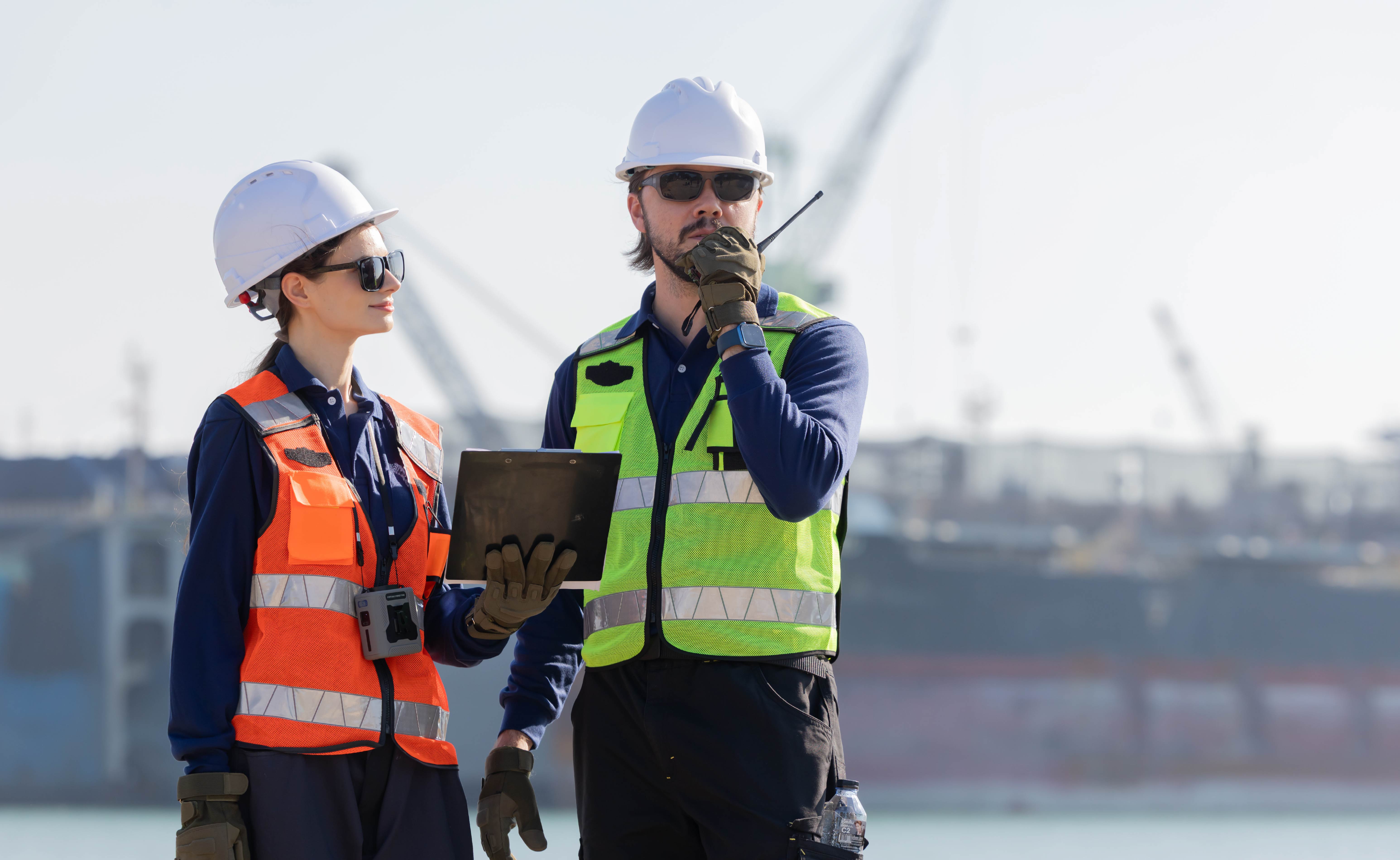 Two maritime workers wearing safety equipment at a port.